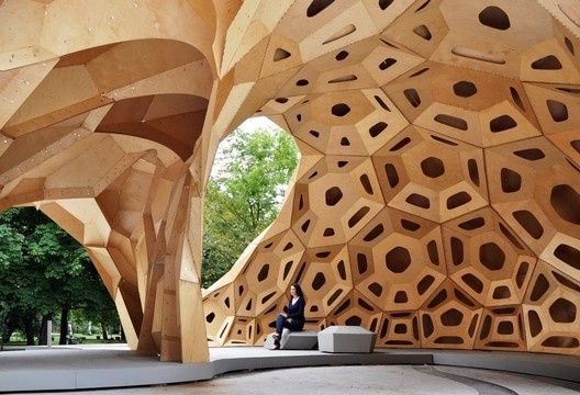 Holzpavillon mit wabenartigen Öffnungen und sitzender Person